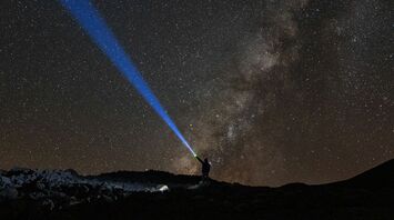 A person shines a blue beam of light into the starry sky over Mauna Kea, Hawaii, with the Milky Way visible in the background