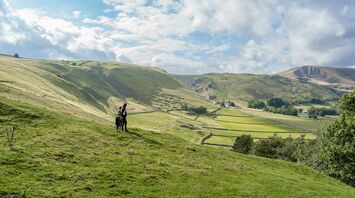 Hikers walking across grassy hills in a remote countryside landscape under a partly cloudy sky