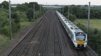 A Greater Anglia train traveling on a multi-track railway through a rural area