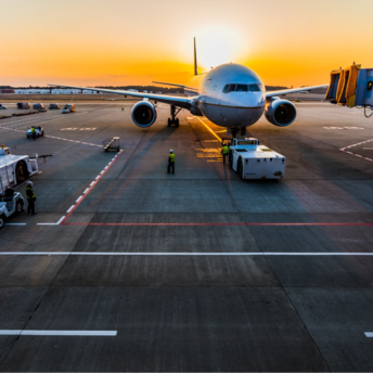 Airplane at airport gate during sunrise with ground crew preparing for departure