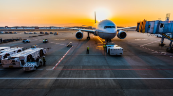 Airplane at airport gate during sunrise with ground crew preparing for departure