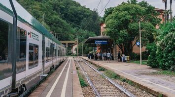 Train at a small Italian railway station surrounded by trees and hills