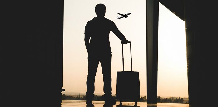 Traveler with suitcase watching airplane take off at airport terminal