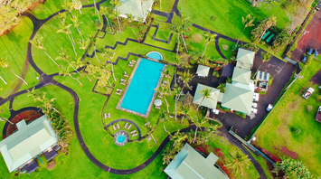 Aerial view of a luxury resort in Maui with a large pool, green lawns, and surrounding villas