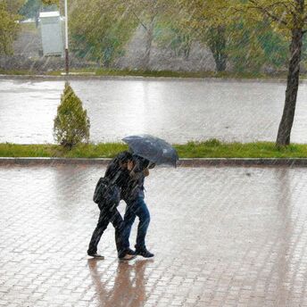 Two people walking with an umbrella during heavy rain on a flooded street