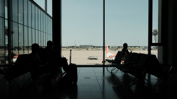 Travelers waiting inside airport terminal with view of parked airplane on the runway