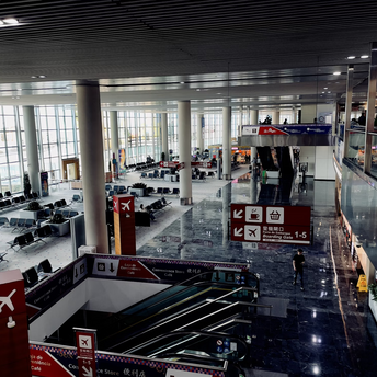 Interior of a modern airport terminal with escalators, gate signs, seating areas, and convenience store signage