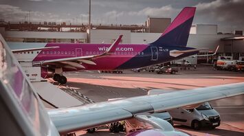 Two Wizz Air aircraft parked at the gate at an airport, with one jet engine visible in the foreground