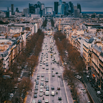 Aerial view of a wide Paris avenue with traffic and pedestrians under dramatic clouds
