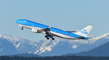 KLM airplane flying over a mountain range with clear blue skies
