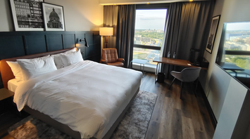 A hotel room featuring a large white bed positioned beside a window