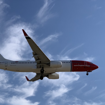 A Norwegian Air plane flying under a blue sky with white clouds