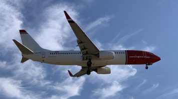 A Norwegian Air plane flying under a blue sky with white clouds