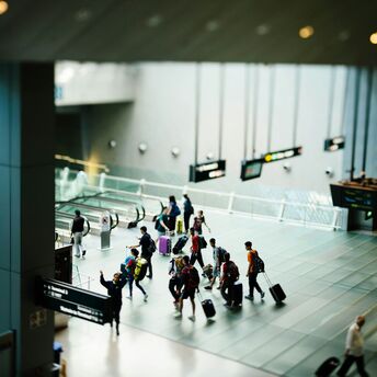 People with luggage walking through a modern airport terminal with electronic signs and escalators