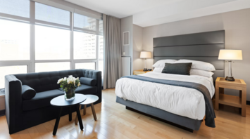 Modern hotel room with large windows, double bed, and a sofa