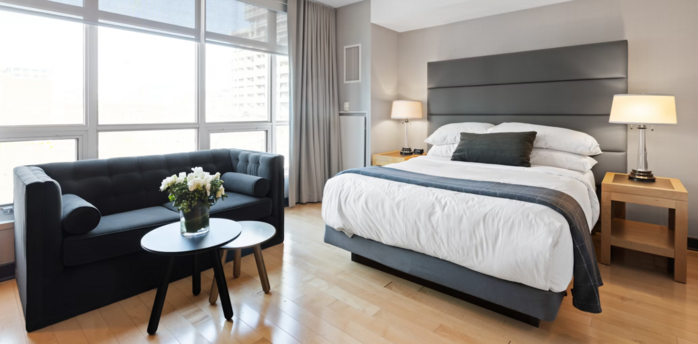 Modern hotel room with large windows, double bed, and a sofa