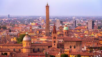 A panoramic view of Bologna at sunset, showcasing historic towers and terracotta rooftops