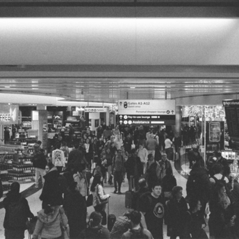 Crowd of passengers in airport terminal with duty-free and flight boards visible