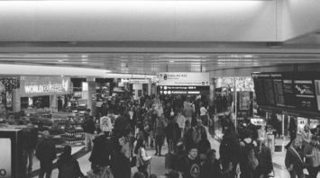 Crowd of passengers in airport terminal with duty-free and flight boards visible