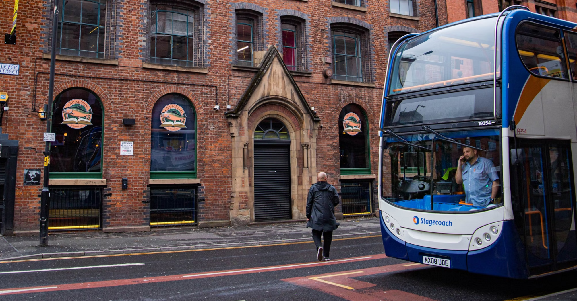 A double-decker Stagecoach bus stops on a street in front of a red-brick building in an urban area