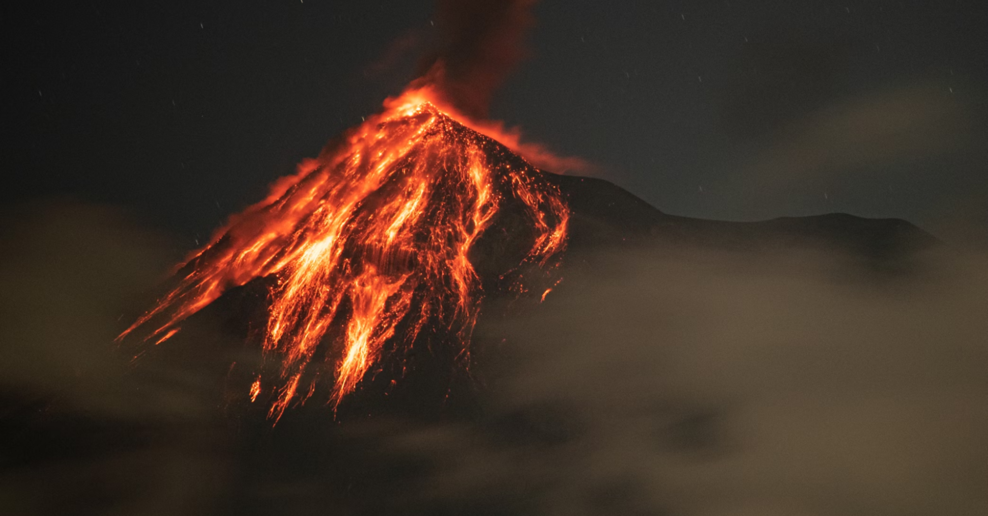 Erupting volcano at night with glowing lava flows and ash plume