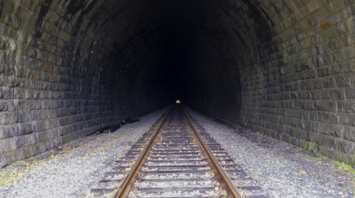 Railway tracks leading into a dark stone tunnel