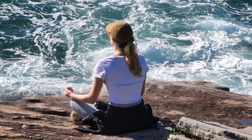 Woman meditating on a rocky shore near the ocean