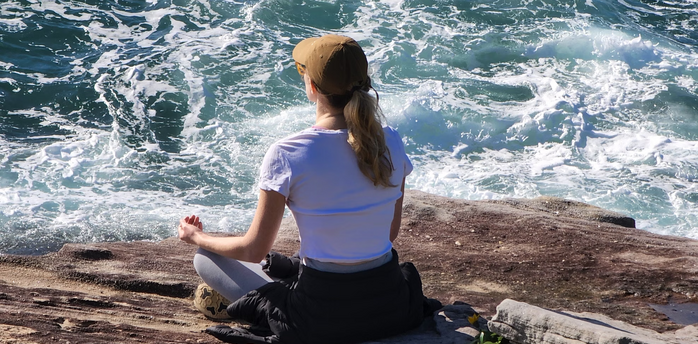 Woman meditating on a rocky shore near the ocean