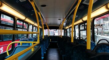 Interior of a public bus with empty seats and yellow handrails