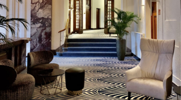 Elegant hotel hallway with patterned carpet, armchairs, and decorative ceiling