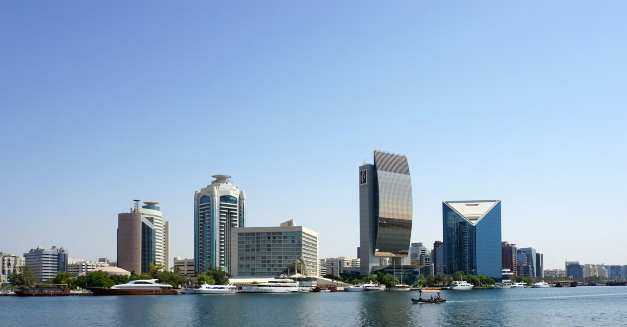 Modern buildings and yachts along Dubai Creek in Deira under a clear blue sky