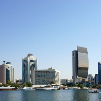 Modern buildings and yachts along Dubai Creek in Deira under a clear blue sky