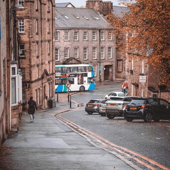 Street view in a historic UK town with a double-decker stagecoach bus, autumn trees, and parked cars