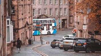 Street view in a historic UK town with a double-decker stagecoach bus, autumn trees, and parked cars