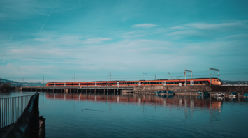 Train crossing a pier bridge over calm water under a clear blue sky