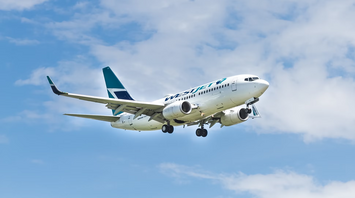 WestJet plane flying through partly cloudy sky