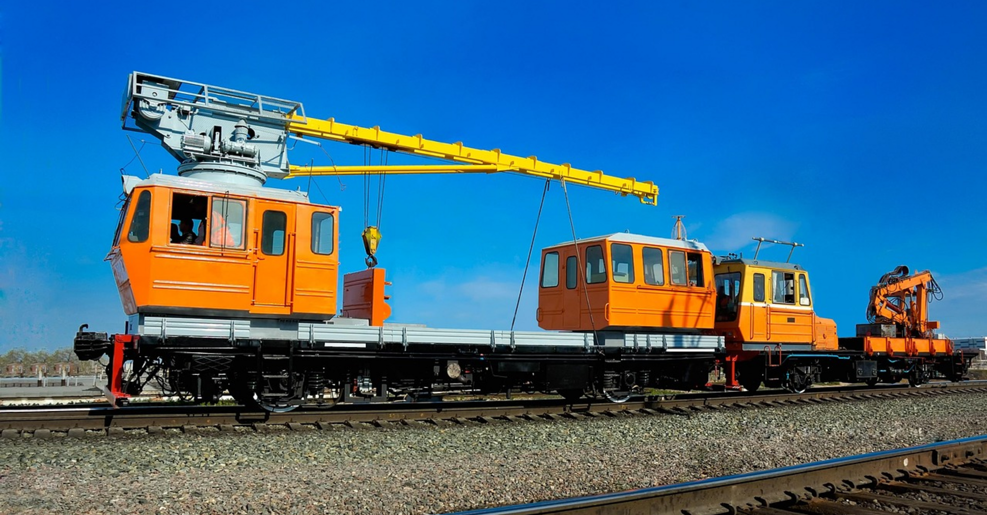 Rail maintenance vehicles on tracks under a clear blue sky
