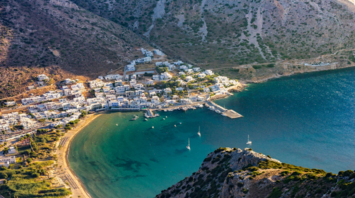 Aerial view of a coastal Greek village surrounded by mountains and a calm turquoise bay
