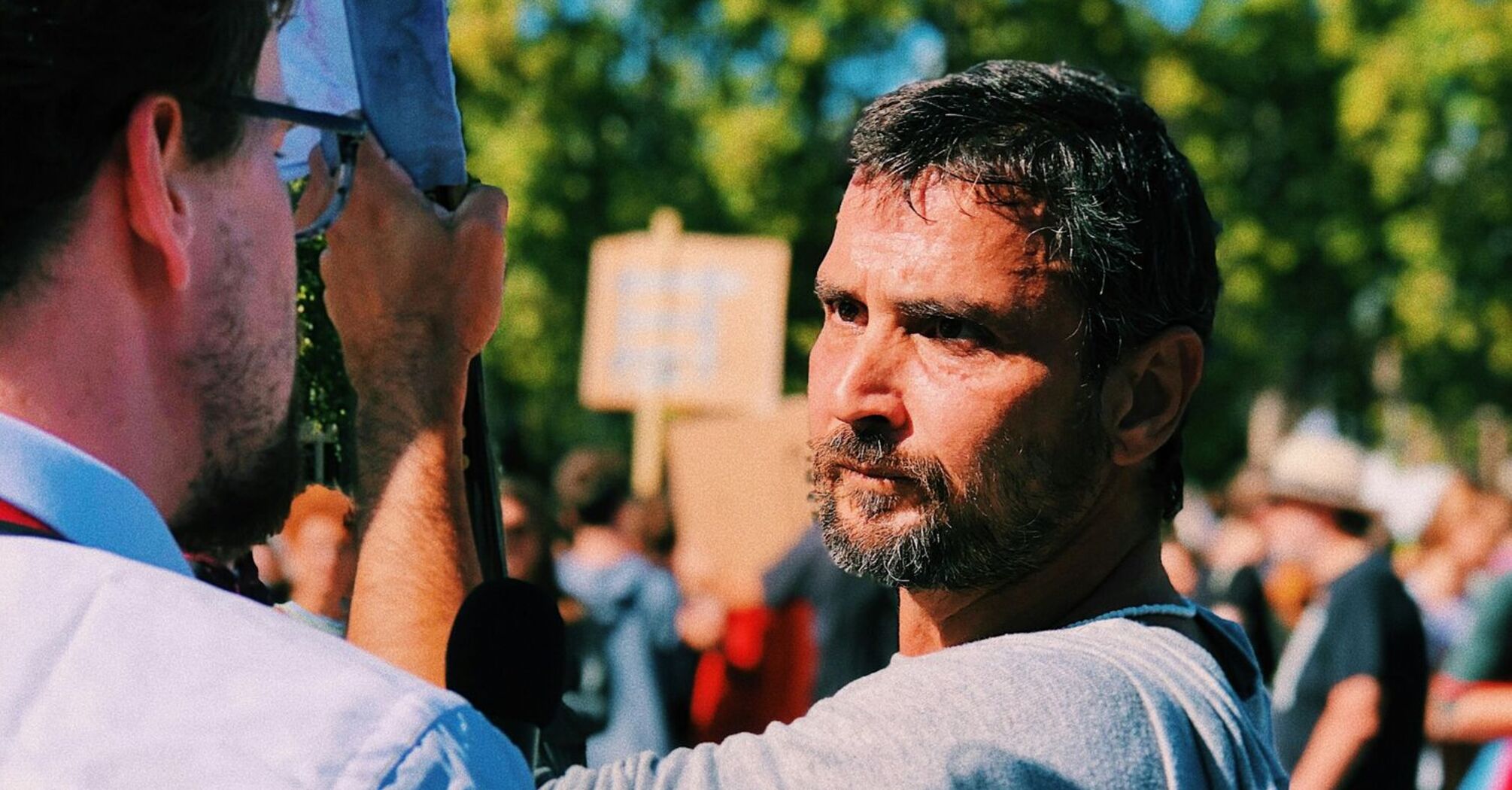 Two men talking during a street protest with signs in the background