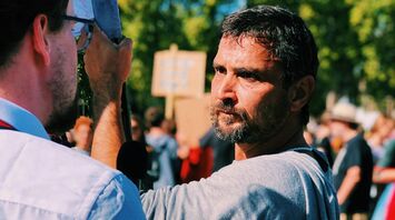 Two men talking during a street protest with signs in the background