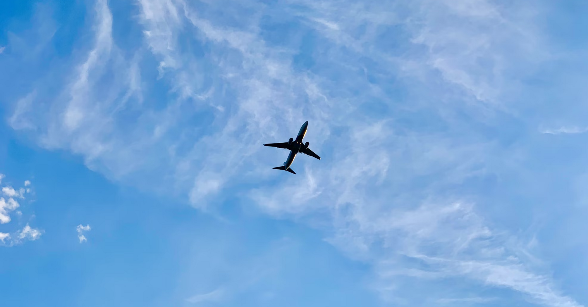 Plane flying in a clear blue sky with light clouds
