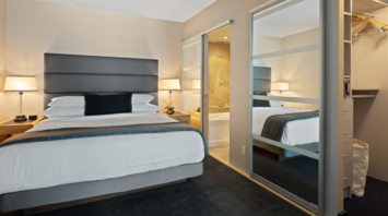 Modern hotel room with king-size bed, nightstands, and mirrored closet