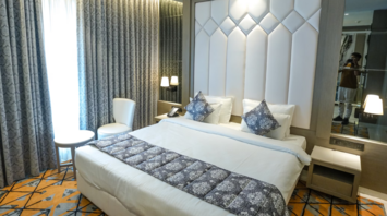 Modern hotel room with large bed, padded headboard, and patterned decor