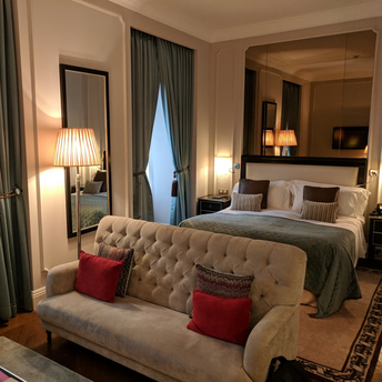 Elegant hotel room with bed, sofa, and tall curtains in soft lighting