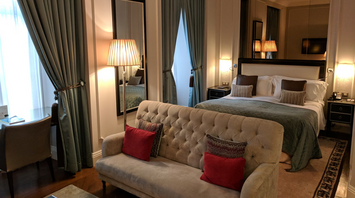 Elegant hotel room with bed, sofa, and tall curtains in soft lighting