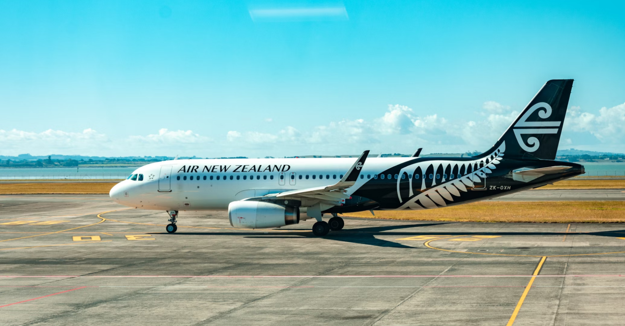 A parked Air New Zealand aircraft on the tarmac under a clear blue sky