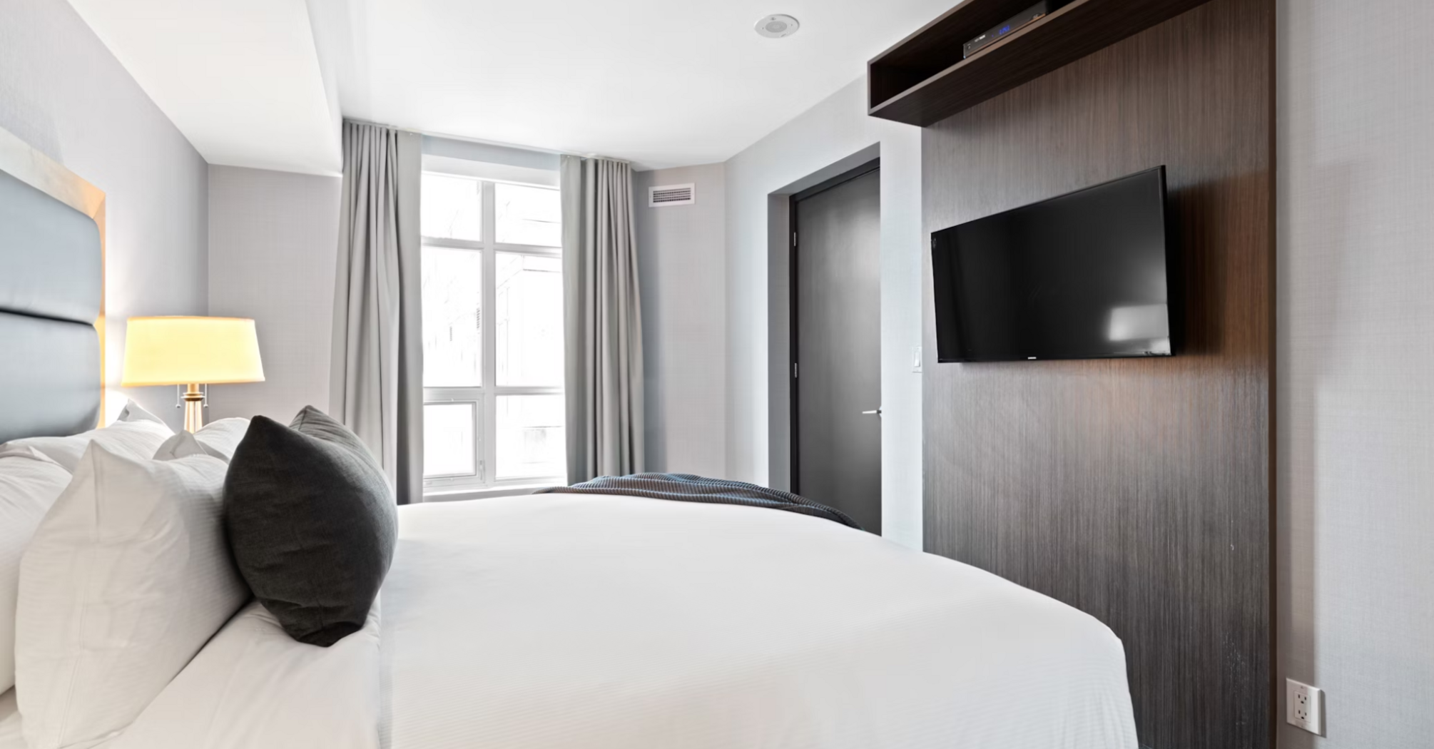 Modern hotel room with large bed, TV, and window with natural light