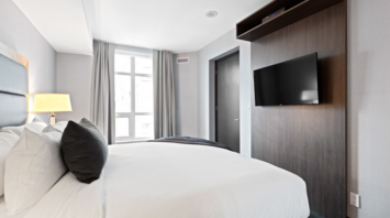 Modern hotel room with large bed, TV, and window with natural light