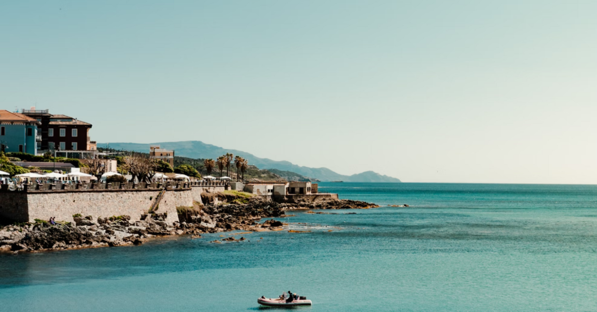 View of Alghero coastline with small boat in turquoise water