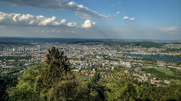Panoramic view of Zurich from a forested hilltop with a river running through the city